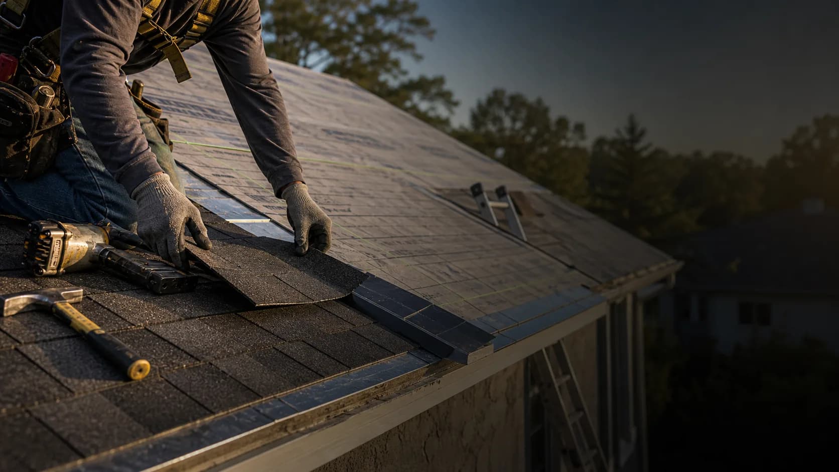 Roofer installing shingles on a residential roof with tools and ladder nearby